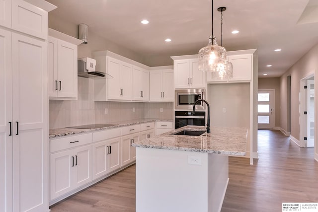 kitchen featuring light wood-type flooring, hanging light fixtures, sink, stainless steel microwave, and a kitchen island with sink