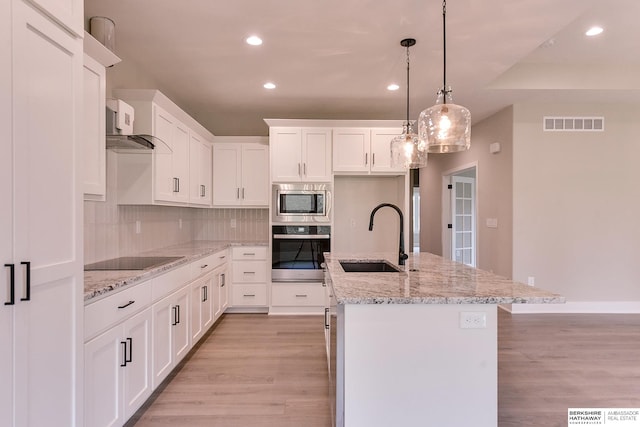 kitchen with white cabinets, sink, an island with sink, light wood-type flooring, and appliances with stainless steel finishes