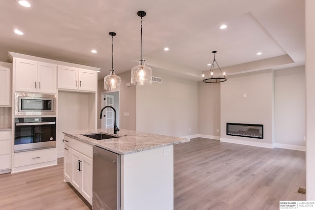 kitchen featuring stainless steel appliances, white cabinetry, sink, hanging light fixtures, and a kitchen island with sink