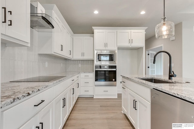 kitchen with wall chimney range hood, appliances with stainless steel finishes, sink, light hardwood / wood-style floors, and white cabinets