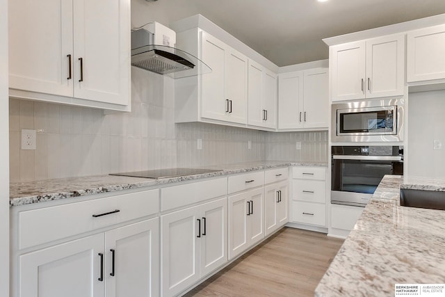 kitchen featuring light stone counters, light wood-type flooring, appliances with stainless steel finishes, exhaust hood, and white cabinets