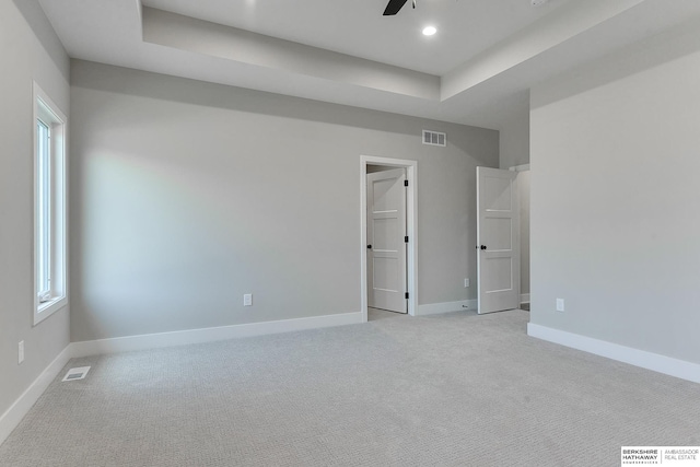 carpeted spare room with a tray ceiling and ceiling fan