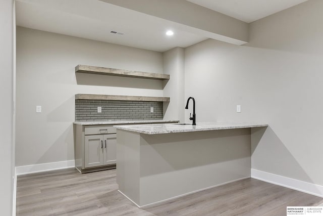 kitchen featuring light hardwood / wood-style floors, light stone counters, kitchen peninsula, decorative backsplash, and sink