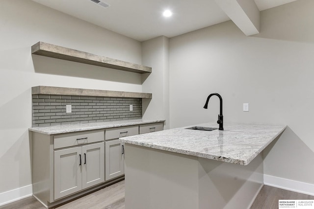 kitchen featuring light hardwood / wood-style floors, sink, tasteful backsplash, light stone countertops, and gray cabinets