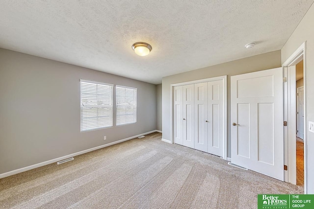 unfurnished bedroom featuring light colored carpet, a textured ceiling, and a closet