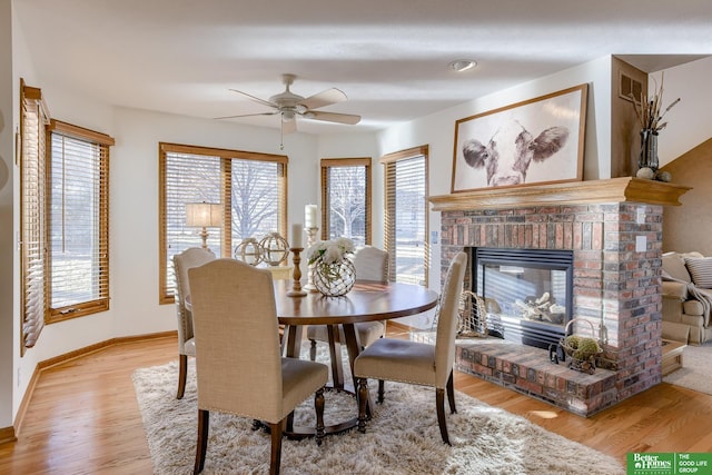 dining room featuring light wood-type flooring, ceiling fan, a healthy amount of sunlight, and a fireplace