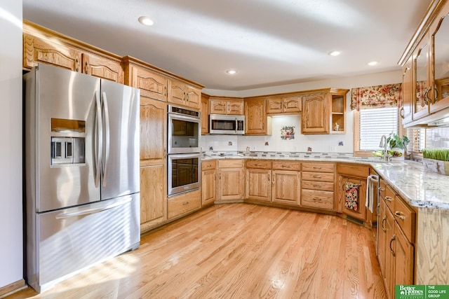 kitchen featuring light hardwood / wood-style floors, sink, light stone counters, appliances with stainless steel finishes, and backsplash