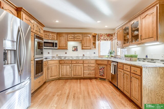 kitchen with decorative backsplash, stainless steel appliances, light stone countertops, and light hardwood / wood-style flooring