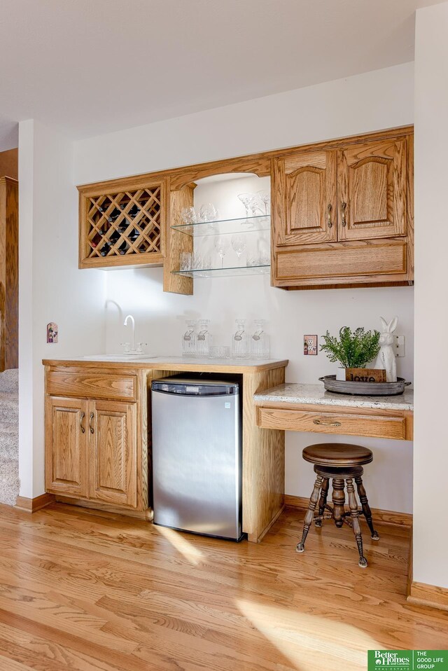 bar featuring sink, stainless steel fridge, and light hardwood / wood-style flooring