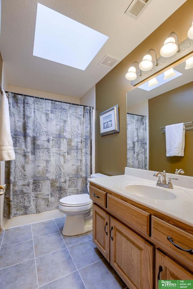 bathroom featuring walk in shower, a skylight, vanity, tile patterned floors, and toilet