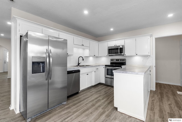 kitchen with light hardwood / wood-style floors, decorative backsplash, sink, white cabinetry, and appliances with stainless steel finishes