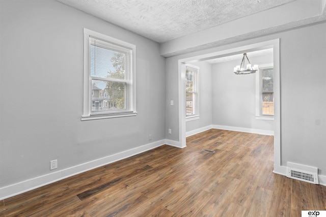 unfurnished dining area featuring wood-type flooring, a textured ceiling, and a chandelier