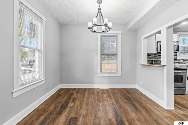 unfurnished dining area featuring dark wood-type flooring, a textured ceiling, and an inviting chandelier