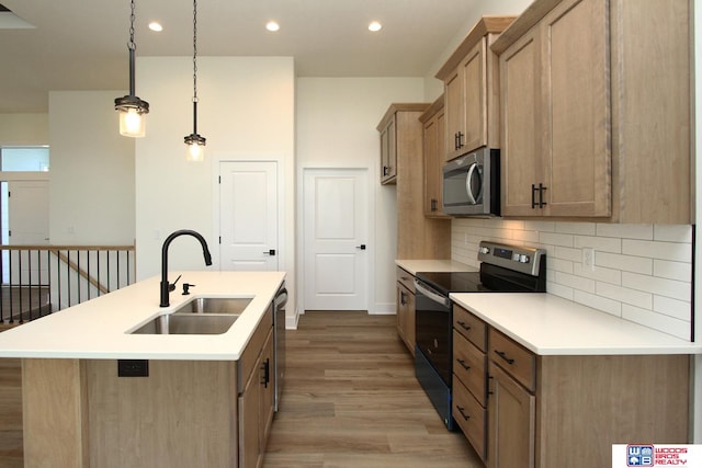 kitchen featuring sink, appliances with stainless steel finishes, hanging light fixtures, a kitchen island with sink, and light hardwood / wood-style flooring