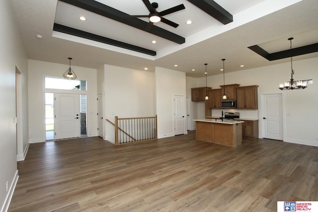 kitchen with pendant lighting, appliances with stainless steel finishes, wood-type flooring, and a kitchen island with sink