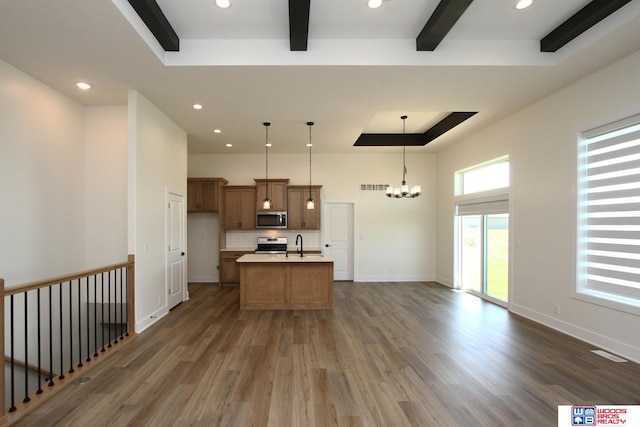 kitchen with appliances with stainless steel finishes, an island with sink, hanging light fixtures, a notable chandelier, and dark hardwood / wood-style flooring