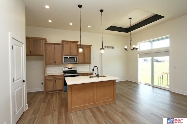 kitchen with appliances with stainless steel finishes, hanging light fixtures, sink, hardwood / wood-style flooring, and a kitchen island with sink