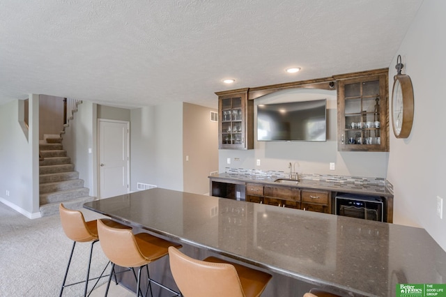 kitchen featuring beverage cooler, light carpet, a textured ceiling, and sink