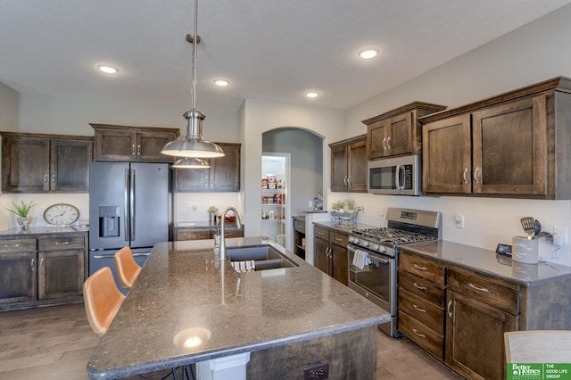 kitchen with stainless steel appliances, dark stone counters, sink, a kitchen island with sink, and pendant lighting