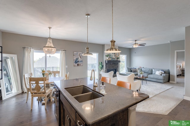 kitchen with a center island with sink, a stone fireplace, a healthy amount of sunlight, and sink