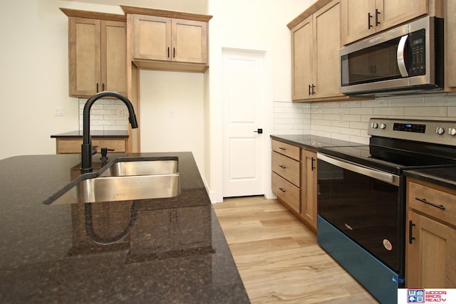 kitchen with light hardwood / wood-style floors, decorative backsplash, sink, appliances with stainless steel finishes, and dark stone countertops