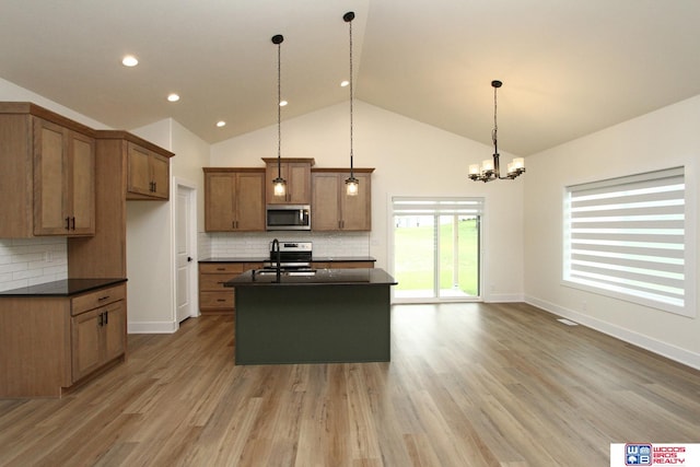 kitchen featuring tasteful backsplash, appliances with stainless steel finishes, pendant lighting, an island with sink, and light hardwood / wood-style flooring