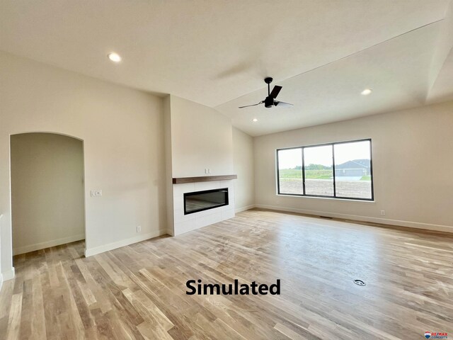 unfurnished living room featuring ceiling fan, light hardwood / wood-style flooring, lofted ceiling, and a tiled fireplace