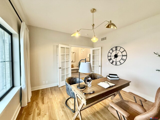 home office with a wealth of natural light, french doors, and light wood-type flooring