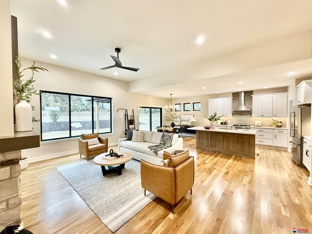 living room with sink, ceiling fan with notable chandelier, and light hardwood / wood-style flooring