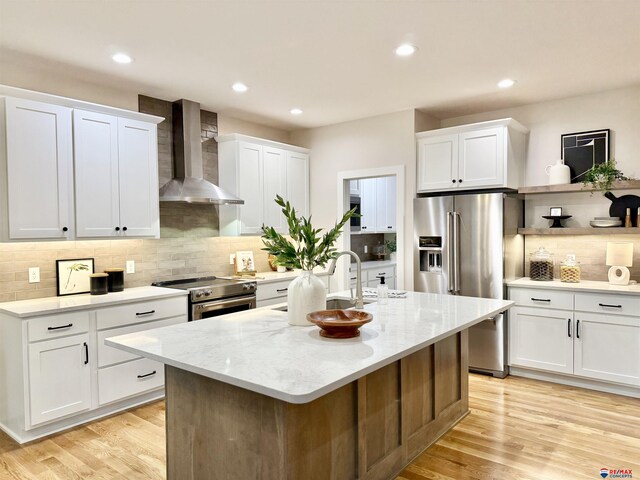 kitchen featuring white cabinetry, high end appliances, a kitchen island with sink, light stone countertops, and wall chimney range hood