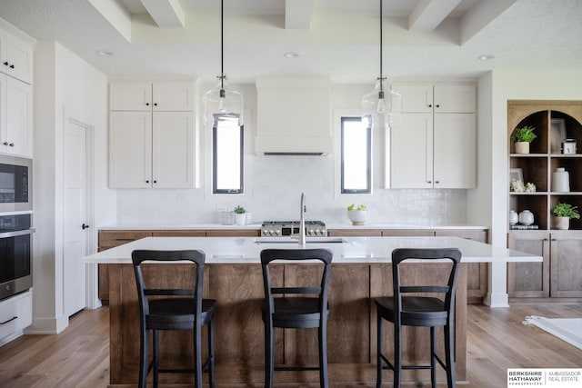 kitchen featuring a kitchen island with sink, white cabinets, oven, and extractor fan