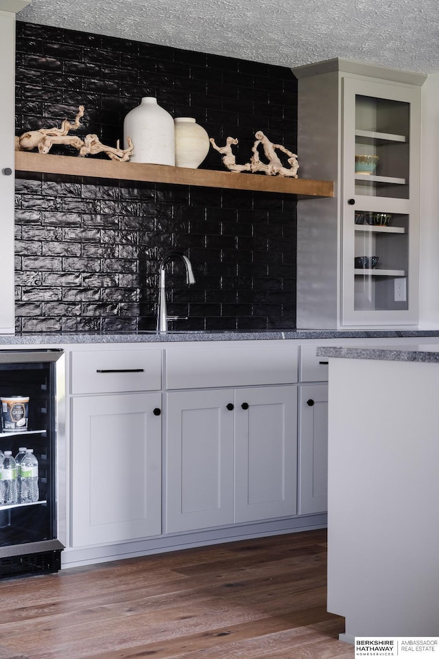 bar with a textured ceiling, beverage cooler, dark wood-type flooring, sink, and white cabinets