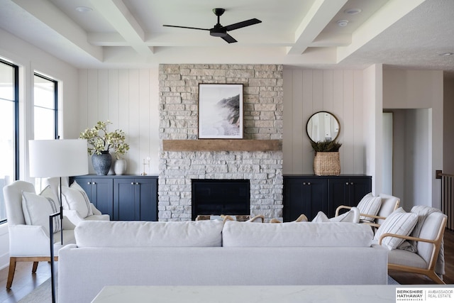 living room with beamed ceiling, ceiling fan, a stone fireplace, and coffered ceiling