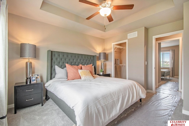 carpeted bedroom with a spacious closet, ceiling fan, a raised ceiling, and a closet