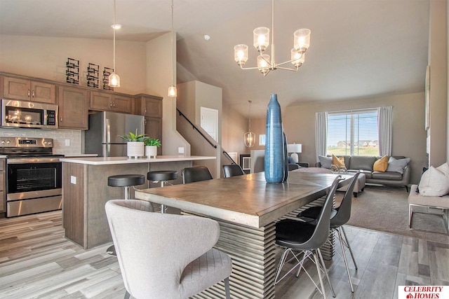 dining area featuring light wood-type flooring, high vaulted ceiling, and a notable chandelier