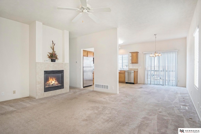 unfurnished living room with ceiling fan with notable chandelier, light carpet, and a tiled fireplace