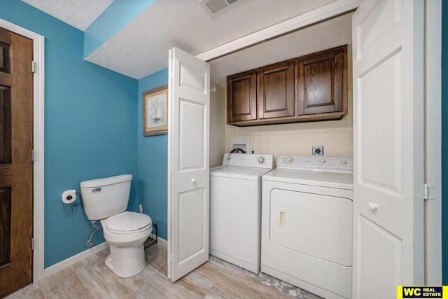 washroom featuring cabinets, light hardwood / wood-style flooring, a textured ceiling, and independent washer and dryer