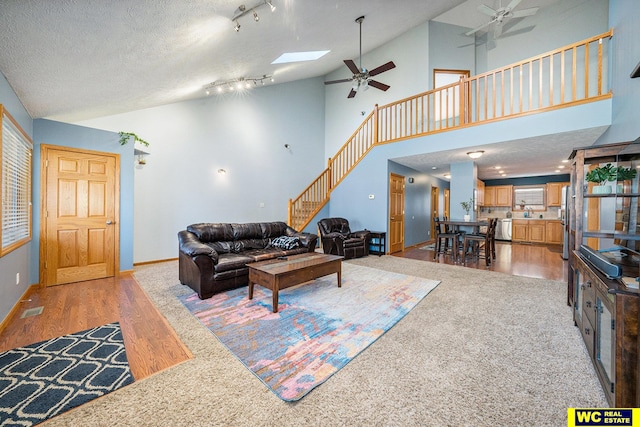 living room featuring hardwood / wood-style floors, a textured ceiling, a skylight, and high vaulted ceiling