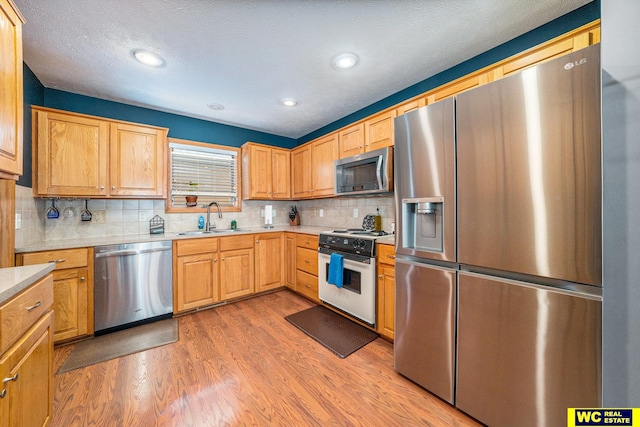 kitchen with tasteful backsplash, appliances with stainless steel finishes, sink, and light hardwood / wood-style floors