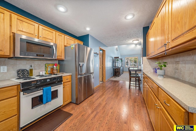 kitchen featuring light hardwood / wood-style floors, vaulted ceiling, a textured ceiling, backsplash, and appliances with stainless steel finishes