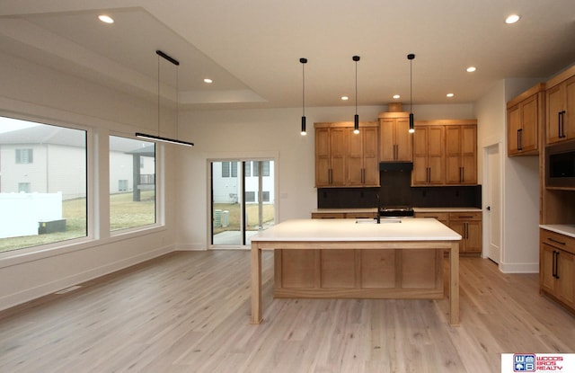 kitchen with light wood-type flooring, decorative light fixtures, and a kitchen island with sink