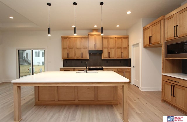 kitchen with hanging light fixtures, light hardwood / wood-style floors, a center island with sink, and sink