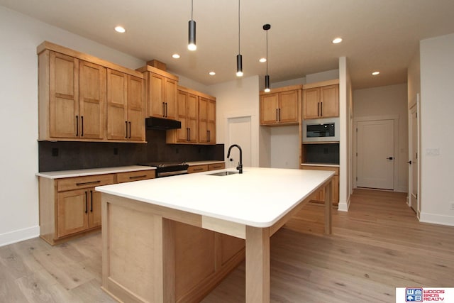 kitchen with stainless steel appliances, light hardwood / wood-style floors, a center island with sink, sink, and hanging light fixtures