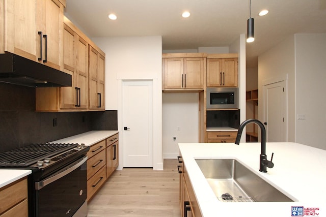 kitchen with appliances with stainless steel finishes, decorative light fixtures, light brown cabinets, sink, and light hardwood / wood-style flooring