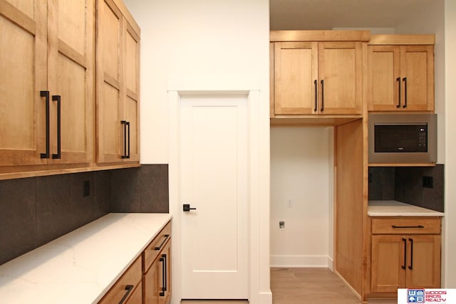 kitchen featuring stainless steel microwave, light hardwood / wood-style floors, and light stone countertops