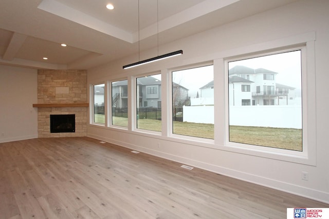 unfurnished living room with a fireplace, a raised ceiling, and light wood-type flooring