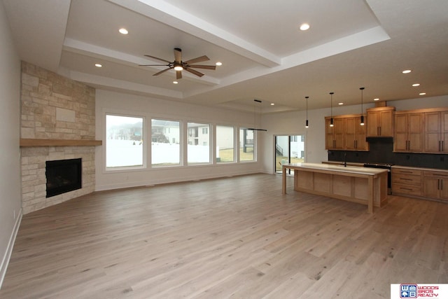 kitchen with a fireplace, light wood-type flooring, decorative light fixtures, ceiling fan, and a kitchen island with sink