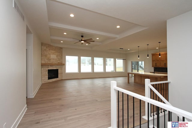 unfurnished living room with a stone fireplace, light wood-type flooring, beamed ceiling, and ceiling fan