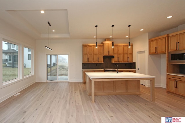 kitchen featuring light hardwood / wood-style floors, a center island with sink, sink, decorative light fixtures, and stainless steel microwave