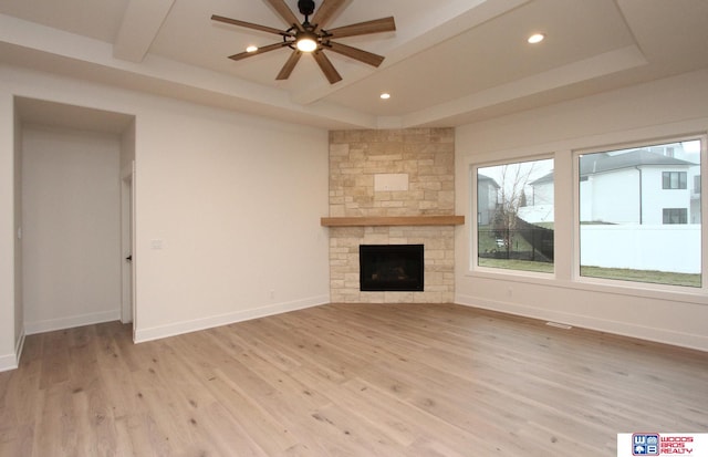 unfurnished living room with light wood-type flooring, a fireplace, ceiling fan, and a raised ceiling